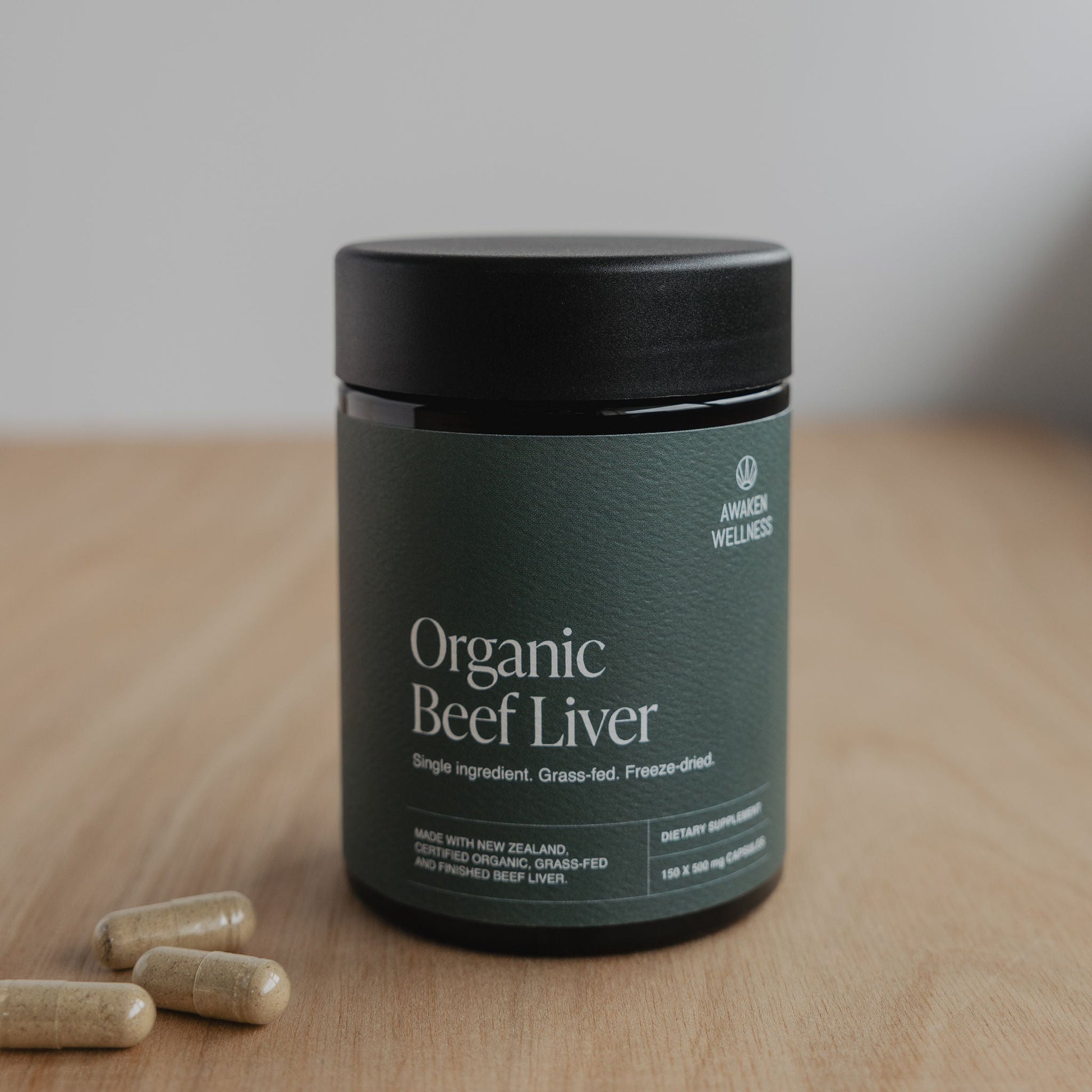 Awaken Wellness Organic Beef Liver capsule bottle on a wooden surface with loose capsules beside it